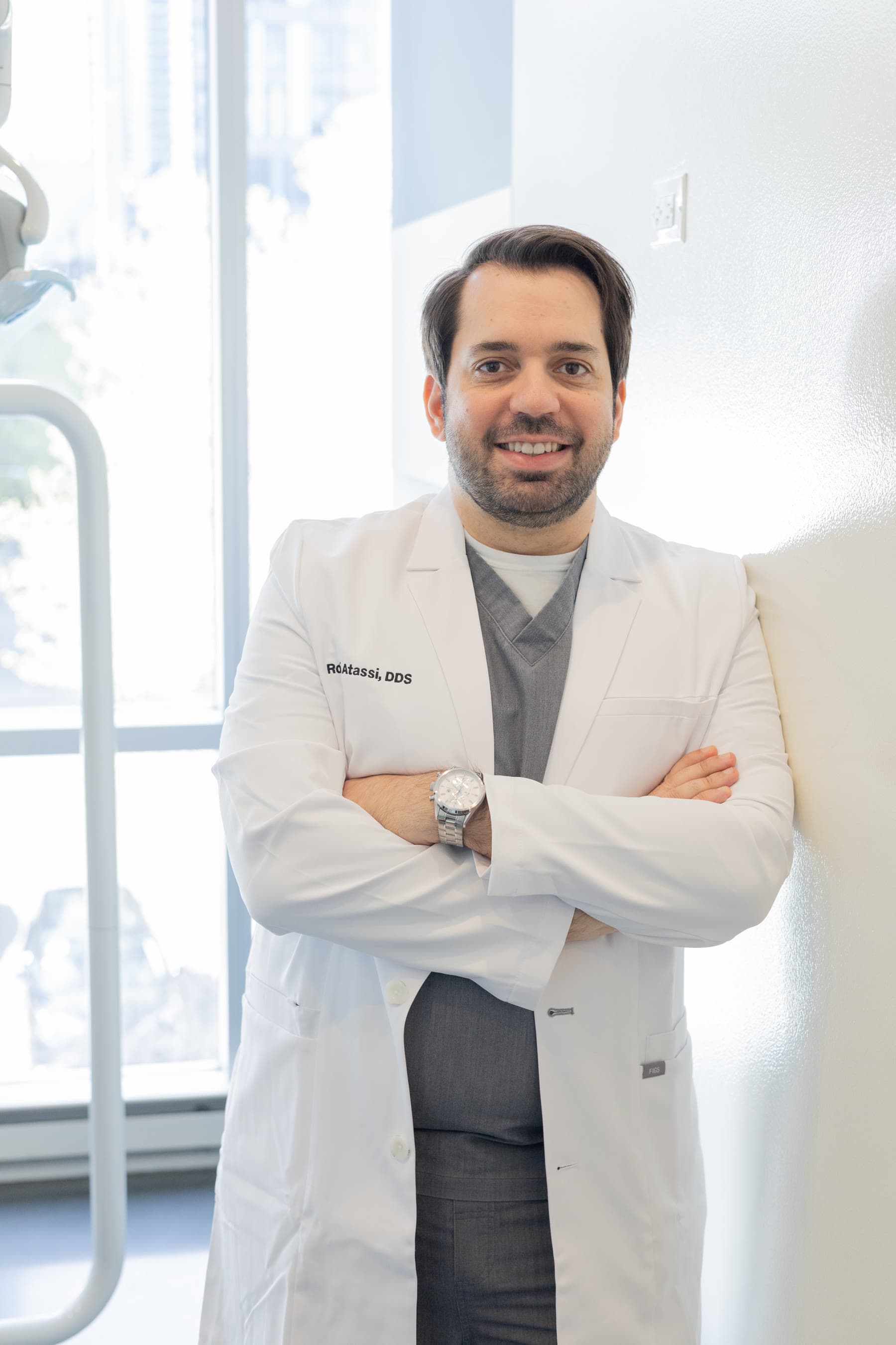 Dr. Atassi, arms crossed, in a treatment room at the window